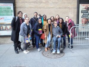 A group of individuals on a New York street staning with Lauren Ridloff, Deaf actress, in the middle. Taylor is off to the left in a blue coat.