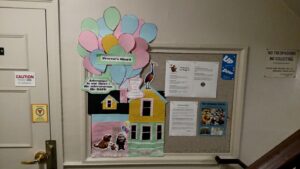 A photo of Taylor's RA bulletin board; on the left, there is a large, colorful house designed after the "Up!" movie. On the right side of the board are informational flyers.
