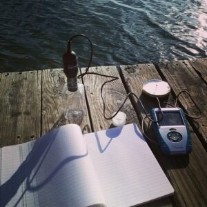 A picture of a notebook and science equipment on a dock overlooking water.